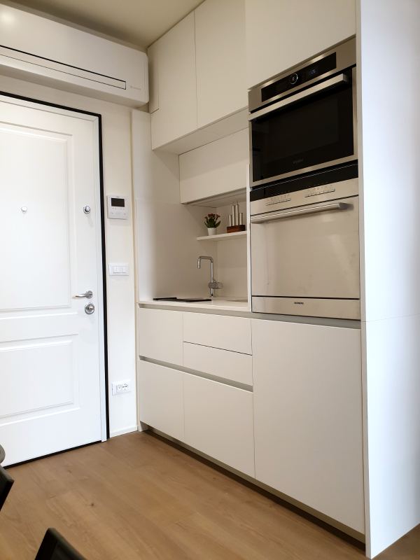 White kitchenette with oven, microwave and sink next to the front door